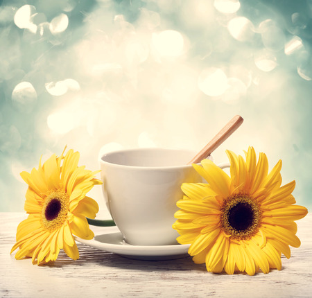 Coffee cup with yellow gerberas over shiny blue backgroundの写真素材