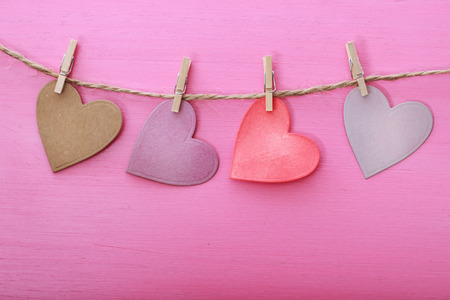 Hand-crafted paper hearts hanging with clothespins over pink wooden boardの写真素材
