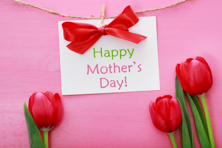 Mothers day card hanging with clothespins over red tulips and pink wooden boardの写真素材