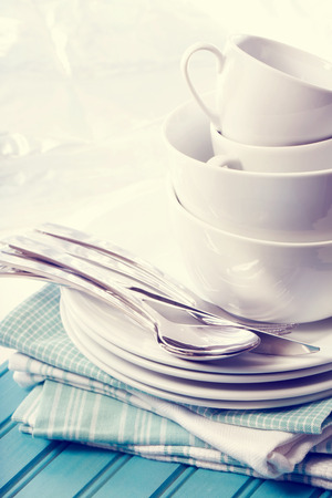 A stack of clean white plates and cups on blue napkins and wooden boardの写真素材
