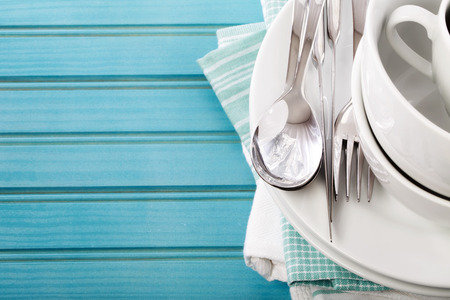 A stack of clean white plates and cups on blue napkins and wooden boardの写真素材