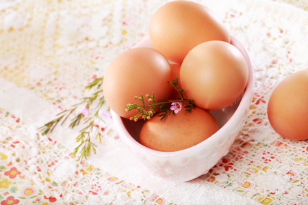 Brown eggs in a porcelain bowl on lace and flower backgroundの写真素材