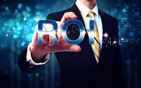 Businessman touching ROI (return on investment) on blue technology backgroundの写真素材