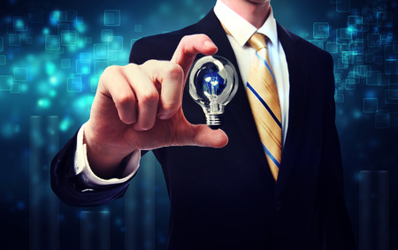 Businessman holding a light bulb over blue shiny backgroundの写真素材