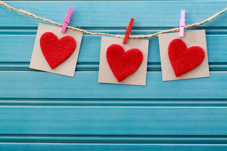Hand-crafted felt hearts hanging with clothespins over blue wooden boardの写真素材