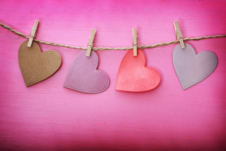 Hand-crafted paper hearts hanging with clothespins over pink wooden boardの写真素材