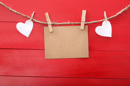 Blank message card and felt hearts with clothespins over red wooden boardの写真素材