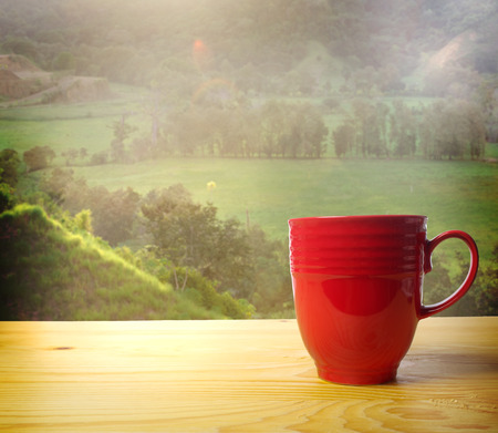 Red coffee mug overlooking a green farmlandの写真素材