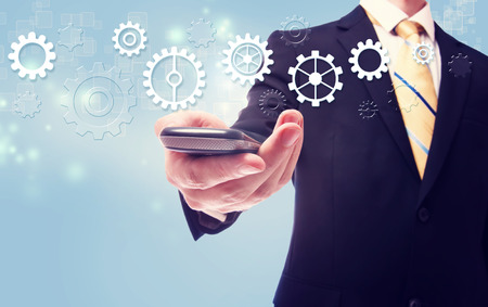 Businessman with gears over a cellphone on light blue backgroundの写真素材