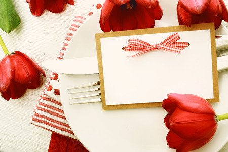 Romantic dinner table setting with blank note card and red tulipsの写真素材