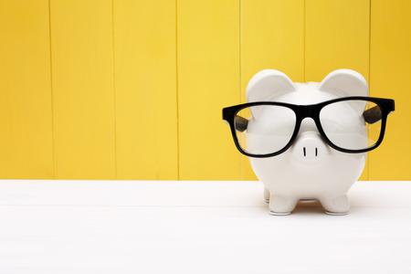 Piggy bank wearing a black glasses over yellow wooden wall