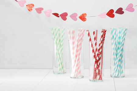 Colorful paper straws with a decorative garland of hearts symbolic of love to celebrate a party for a festive romantic occasion, with copyspace for your invitation or greetingの写真素材