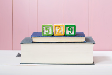 529 college savings plan concept with textbooks stacked in front of a pink wooden background with...
