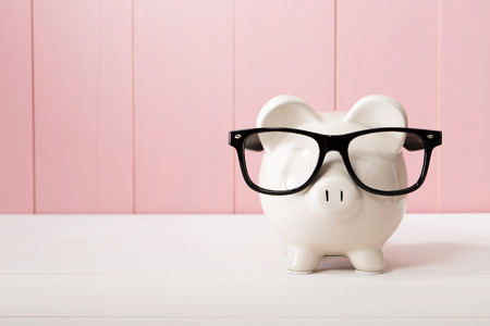 Piggy bank with black glasses on pink wooden wall