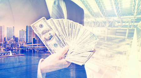 Double exposure of businessman displaying spread of cash on blurred city backgroundの写真素材