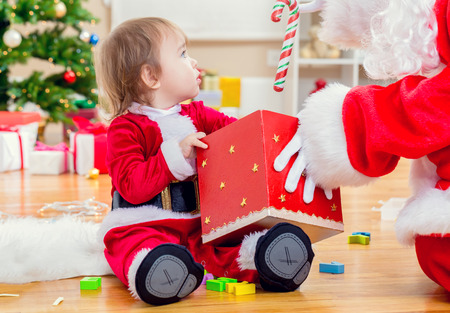 Little toddler girl receiving a gift from Santa Claus by the Christmas treeの写真素材