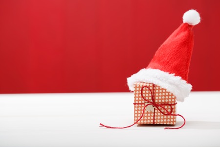Christmas little gift box with Santa hat on red colored wooden boardの写真素材