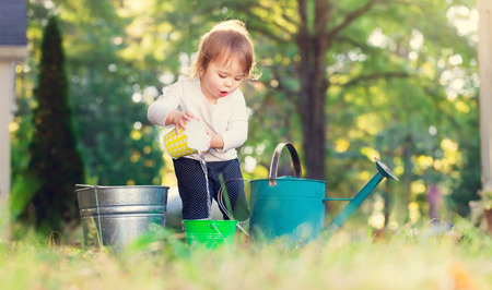 Happy toddler girl playing with watering cans outsideの写真素材