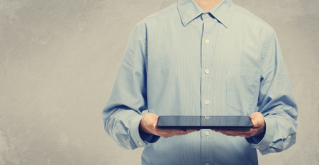 Young man holding a tablet computer on gray colored backgroundの写真素材