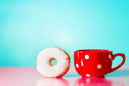 White donut with big red mug on a pastel blue and pink background