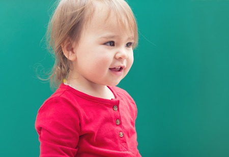 Happy toddler girl smiling in front of a green chalkboardの写真素材