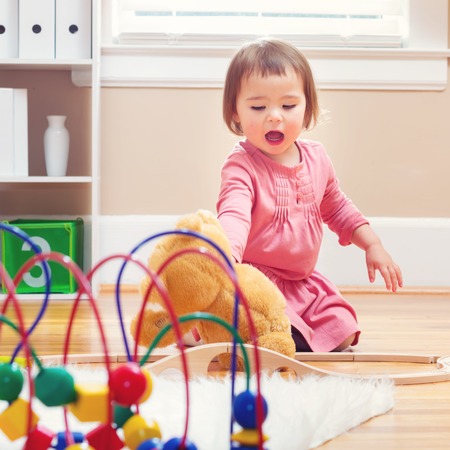 Happy toddler girl playing with her teddy bear at houseの写真素材