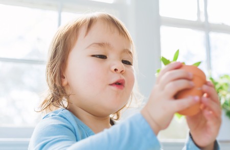Happy toddler girl playing with little potted plants in her house