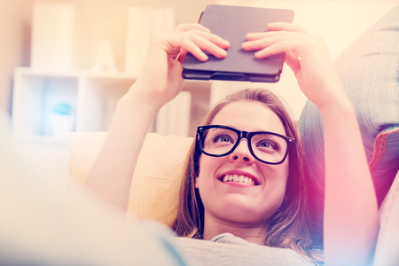 Happy young woman reading an e-book on her couch at homeの写真素材