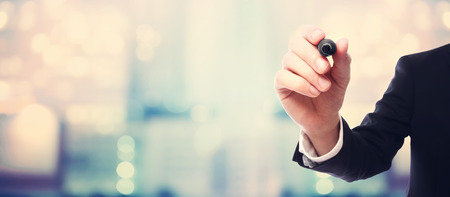 Businessman drawing something with a black maker on blurred abstract backgroundの写真素材