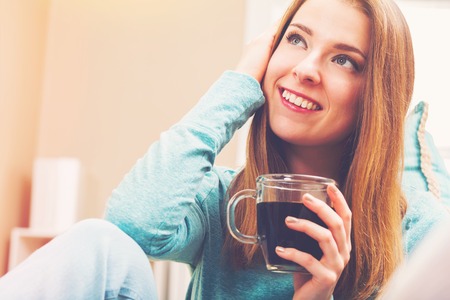 Happy young woman drinking coffee on her couchの写真素材