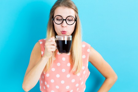 Happy young woman drinking coffee on blue backgroundの写真素材