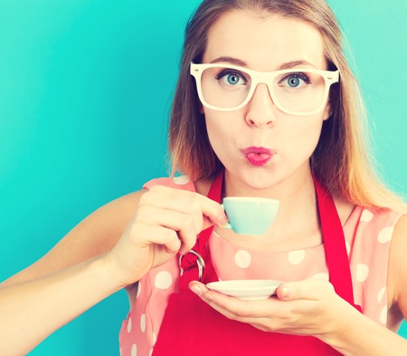 Happy young woman drinking coffee on blue backgroundの写真素材