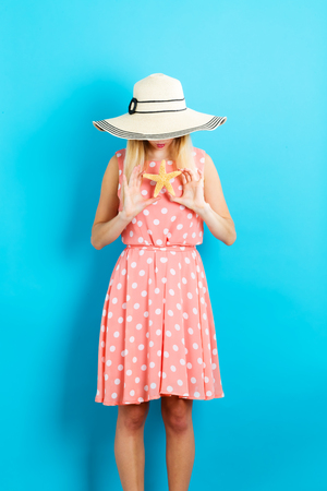 Happy young woman holding a starfish on blue backgroundの写真素材