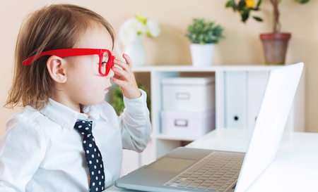 Smart little toddler girl wearing big red glasses while using her laptopの写真素材