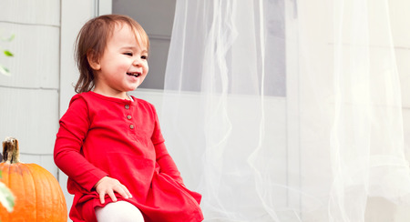 Happy toddler girl sitting on her front steps in autumnの写真素材