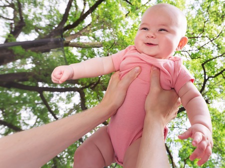 Happy infant baby girl being held up in the air by her parentの写真素材