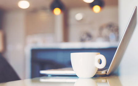 Open slim metal laptop computer beside white coffee mugの写真素材