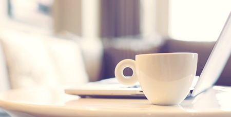 White coffee mug beside laptop computer for early morning work conceptの写真素材