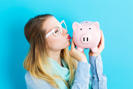 Young woman with a piggy bank on a blue backgroundの写真素材