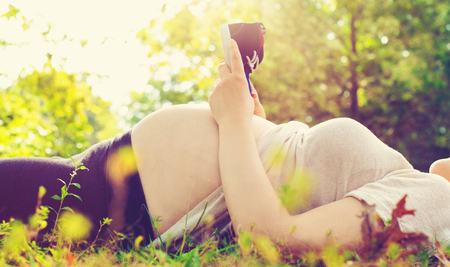 Pregnant woman outside holding baby shoes to her bellyの写真素材
