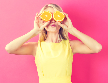 Happy young woman holding oranges halves on a pink backgroundの写真素材