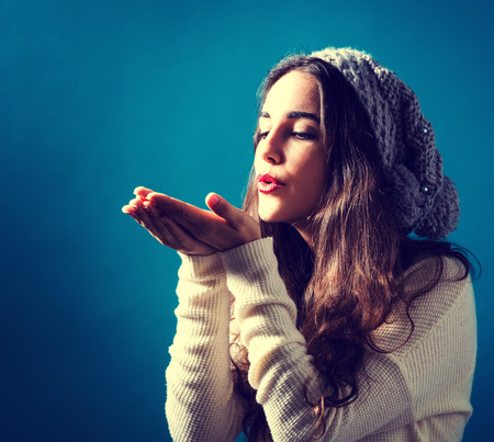 Happy young woman with winter clothes blowing a kissの写真素材