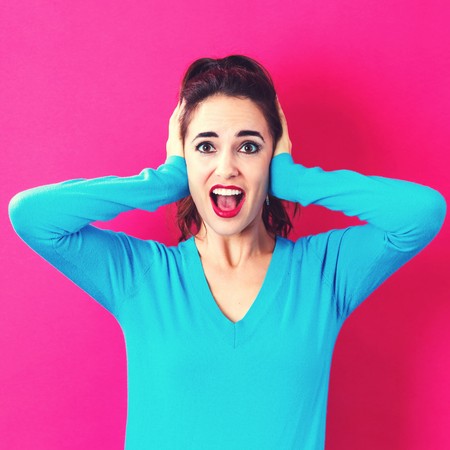 Young woman blocking her ears on a pink backgroundの写真素材