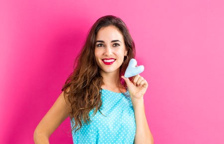 Happy young woman holding a heart cushion on a pink backgroundの写真素材