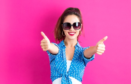 Happy young woman giving thumbs up on a pink backgroundの写真素材