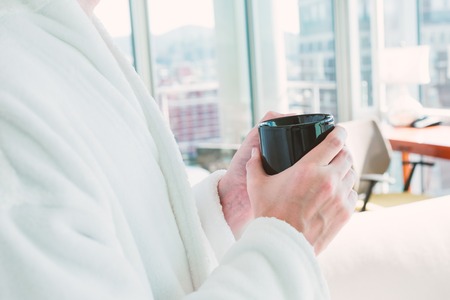 Man in a bathrobe with a cup of coffee in a brightly lit modern interior living spaceの写真素材