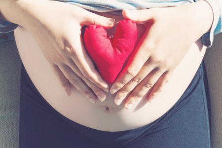 Pregnant woman holding a heart shaped cushion on her bellyの写真素材