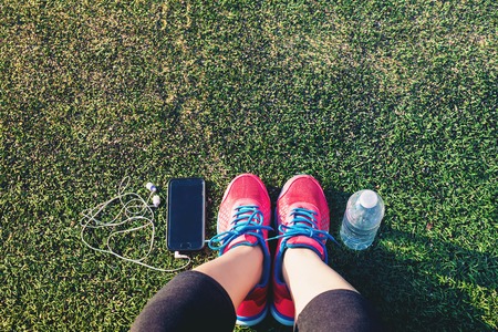 Female runner looking down at her feet, phone and water bottle in a fieldの写真素材