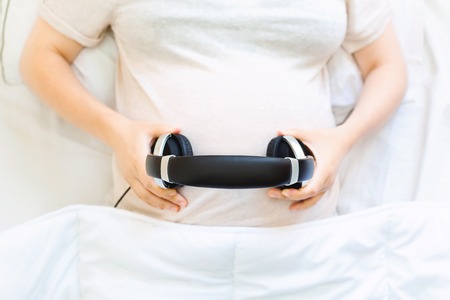 Pregnant young woman with headphones on her belly playing music for her babyの写真素材