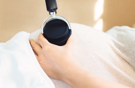Pregnant young woman with headphones on her belly playing music for her babyの写真素材
